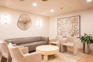 Warm reception lounge with sofa, armchairs, plants, artwork, and relaxed atmosphere at Greenwich Dental Studio clinic.