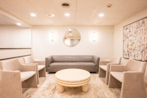 Modern lounge area with curved seating, round table, mirror, and soft lighting at Greenwich Dental Studio.