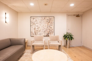 Comfortable waiting room with sofa, chairs, round table, artwork, and plant at Greenwich Dental Studio clinic.